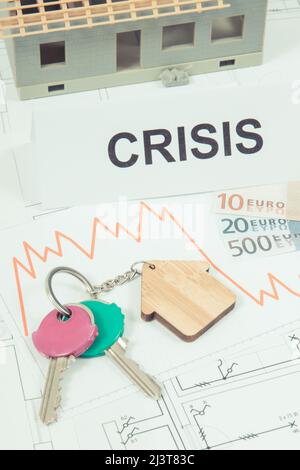 Schlüssel mit Hausform, Währungen Euro, Abwärtsgraphen und Inschrift Krise auf elektrischen Baudiagramme des Hauses. Immobilienkrise Stockfoto