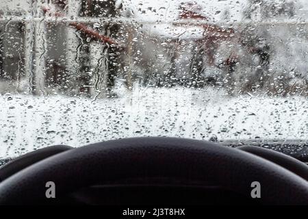 Tropfen von geschmolzenen Schneeflocken auf der Windschutzscheibe eines Autos. Stockfoto