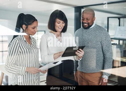 Die Leistungsbeurteilung sieht gut aus. Eine Kurzaufnahme einer vielfältigen Gruppe von Geschäftsleuten, die im Büro zusammenstehen und während einer ein Tablet verwenden Stockfoto
