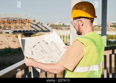 Ernst beschäftigter Mann in Hardhat und grüner Weste, der auf der Baustelle des Wohngebäudes arbeitet Stockfoto