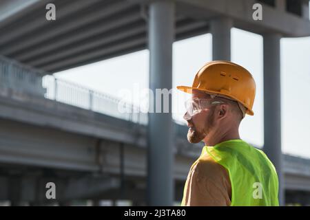 Hintergrundbeleuchtetes Seitenbild eines Bauarbeiters mit Hardhut, der im Hintergrund gegen den Himmel steht und den Raum kopiert Stockfoto