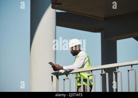 Seitenansicht Porträt eines jungen schwarzen Ingenieurs mit Hardhut auf der Baustelle gegen den Himmel, Kopierraum Stockfoto