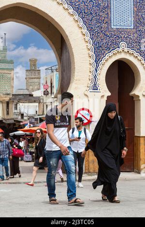 Fes, Marokko.  Bab Boujeloud, Eingang zum Fes El-Bali, der alten Stadt.  Frau in konservativen schwarze Djellaba begleitet von Mann in Levis und Western-sty Stockfoto