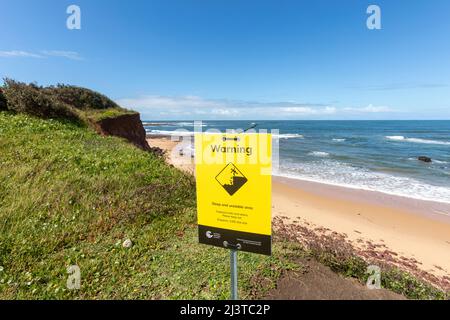 Warnschild für instabiles Gelände und langen Fall an der Long Reef Landspitze mit steilem Abfall zum Strand, Sydney, NSW, Australien Stockfoto