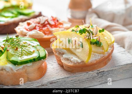 Crostini mit Ricotta, Apfel und Mikrogrün, Feta, Gurke und Dill auf hellem Hintergrund. Stockfoto