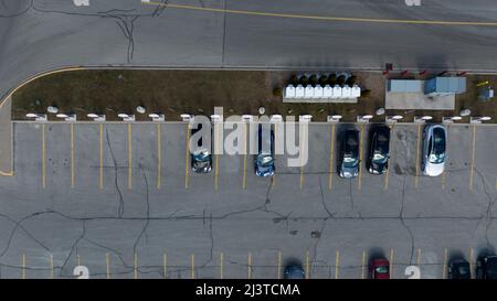 Eine direkte Luftaufnahme über einer Tesla Supercharger-Station, Autos werden geparkt gesehen, während des Tages aufgeladen. Stockfoto