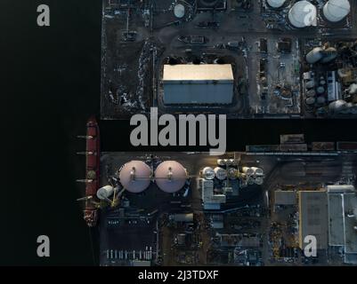Eine direkte Ansicht von oben auf eine landwirtschaftliche Anlage in einem Hafen am Wasser, da ein Frachtschiff angedockt ist. Stockfoto