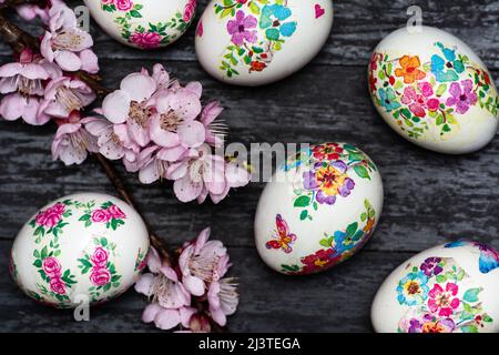 Weiße Ostereier mit Decoupage-Technik mit floralen Motiven und einem blühenden Ast auf schwarzem rustikalem Hintergrund. Stockfoto