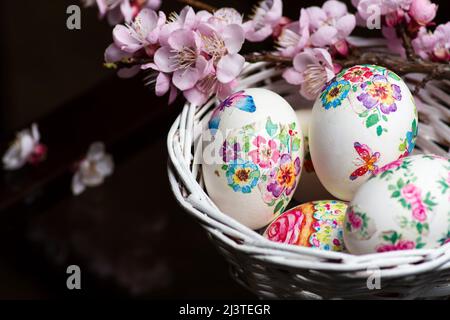 Weiße Ostereier mit Decoupage-Technik mit floralen Motiven und einem blühenden Ast auf schwarzem rustikalem Hintergrund. Stockfoto