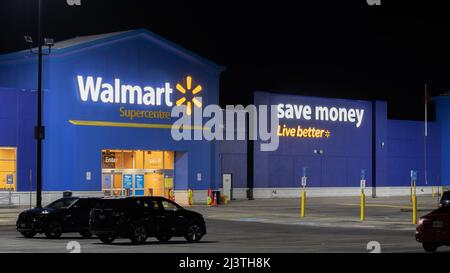 Die Vorderseite eines Walmart Superstore ist nachts abgebildet, ihr berühmter Slogan „Save Money, Live Better“ ist an der Seite des Gebäudes zu sehen. Stockfoto