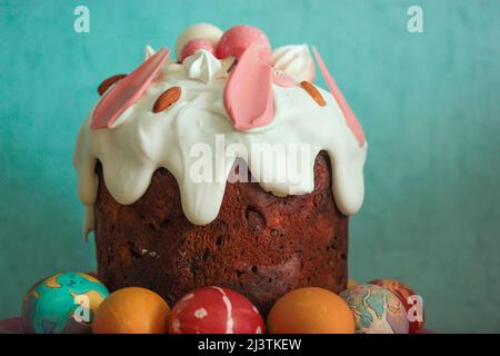 Osterkuchen mit weißer Glasur, die auf blauem Hintergrund herunterfließt. Handbemalte bunte Ostereier. Traditionelles Osterdessert auf festlichem Tisch. Stockfoto