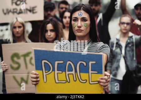 Friedensaktivisten protestieren gegen den Krieg gegen die Ukraine. Konzentrieren Sie sich auf eine junge Frau, die ein Plakat mit der Flagge und dem Weltfrieden hält. Stockfoto