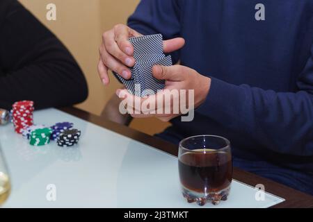 Die Hände des Mannes mischen Karten in einem Pokerspiel. Chips, Karten, Glas Whiskey auf dem Tisch mit Spiegelung. Poker Club. Stockfoto