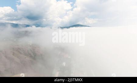 Draufsicht auf dichte Wolken am Himmel mit Berggipfeln. Aktion. Fliegen über weiße Wolken auf dem Hintergrund des himmlischen Horizonts mit Berg. Panorama von Stockfoto