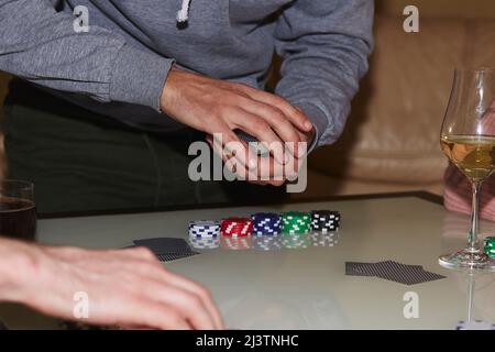 Man's Hands shuffling Karten in einem Poker-Spiel. Chips, Karten, ein Glas Champagner auf dem Tisch mit Spiegelung. Poker Club. Stockfoto