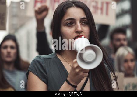 Porträt einer Aktivistin bei einem protestmarsch mit einem Megaphon mit Krähen hinter sich Stockfoto