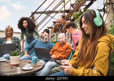 Eine Gruppe von Studenten, die auf der Campus-Terrasse mit digitalen Geräten wie Laptops und Smartphones zusammenarbeiten und gemeinsam im Freien arbeiten Stockfoto