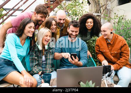 Junge Studenten vor einem Laptop, der Inhalte vom Smartphone aus ansieht, während sie online streamen. Konzept der Überprüfung der Online-Visualisierung aus der Zelle Stockfoto