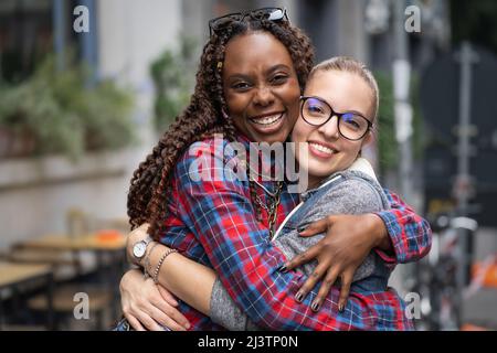 Portrait von zwei interracial besten Freundinnen, die sich auf den Straßen umarmen. Studenten Freundinnen Spaß zusammen. Stockfoto