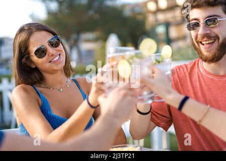 Eine Gruppe junger Leute mit Sonnenbrillen, die im Sommer im Café im Freien toasten Stockfoto