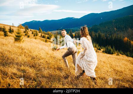 Glücklich wunderschöne Braut und Bräutigam zu Fuß in Sonnenlicht halten Hände, boho Brautpaar Stockfoto