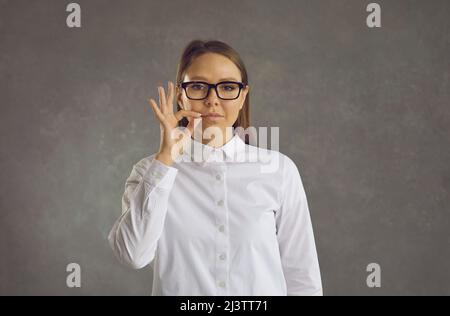 Eine junge, selbstbewusste, geheime Frau zeigt ein Zeichen des Schweigens, indem sie ihren Mund mit einem Schloss schließt. Stockfoto