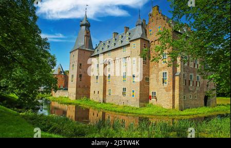 Blick über den grünen Park mit Graben auf das mittelalterliche holländische Wasserschloss aus dem 14.. Jahrhundert vor dem blauen Sommerhimmel - Kasteel Doorwerth bei Arnhem, Niederlande Stockfoto