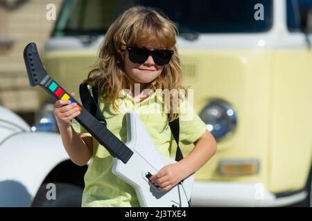 Netter Junge singt und spielt auf der E-Gitarre mit lustigen Emotionen. Musikinstrumente für Kinder. Stockfoto