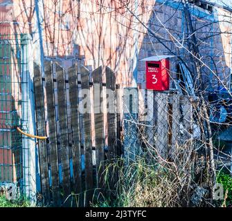 Roter Briefkasten, mit weißen Buchstaben, schriftlicher Adresse und Hausnummer auf einem Holzzaun. Stockfoto