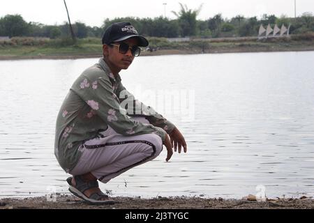 Kleiner Junge, der am Strand posiert. Netter lächelnder, glücklicher 11-jähriger Junge am Flussufer, der die Kamera anschaut. Kinderportrait im Freien. Stockfoto