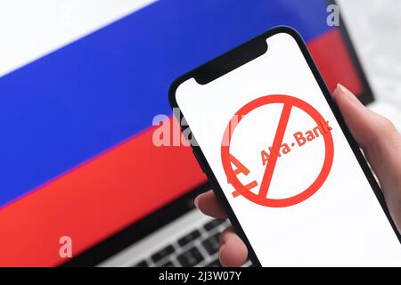 SPB, Russland - 8. April 2022: Alfabank und Sanktionen. Blockierte russische Bank, Logo und Ban-Symbol auf Handy-Bildschirm und Flagge Hintergrund Stockfoto