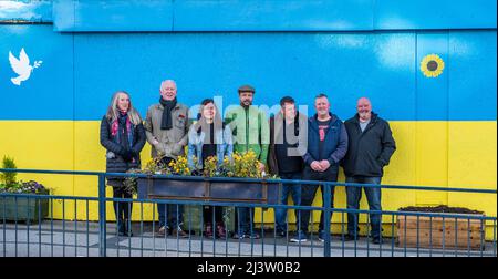 Starbeck, Harrogate, Großbritannien. 10. April 2022. Mitglieder der Starbeck Community Group Jill De Witt, Andrew Hart, Lucky Hubbard, Nik Mills, John Keane, David Stead und Colin Wilson fotografierten vor einer 40 Meter langen ukrainischen Flagge, die sie über dem einst schönen und heute verkommenen Harper-Gebäude in der Starbeck High Street gemalt hatten. Dies ist eines von vielen Projekten, an denen sie arbeiten, um ihre lokale Gemeinschaft zu beleben und zu motivieren. Kredit: ernesto rogata/Alamy Live Nachrichten Stockfoto