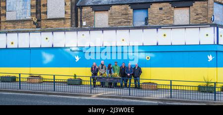 Starbeck, Harrogate, Großbritannien. 10. April 2022. Mitglieder der Starbeck Community Group Jill De Witt, Andrew Hart, Lucky Hubbard, Nik Mills, John Keane, David Stead und Colin Wilson fotografierten vor einer 40 Meter langen ukrainischen Flagge, die sie über dem einst schönen und heute verkommenen Harper-Gebäude in der Starbeck High Street gemalt hatten. Dies ist eines von vielen Projekten, an denen sie arbeiten, um ihre lokale Gemeinschaft zu beleben und zu motivieren. Kredit: ernesto rogata/Alamy Live Nachrichten Stockfoto