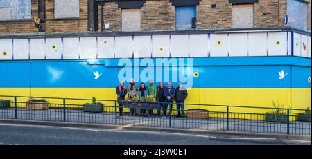 Starbeck, Harrogate, Großbritannien. 10. April 2022. Mitglieder der Starbeck Community Group Jill De Witt, Andrew Hart, Lucky Hubbard, Nik Mills, John Keane, David Stead und Colin Wilson fotografierten vor einer 40 Meter langen ukrainischen Flagge, die sie über dem einst schönen und heute verkommenen Harper-Gebäude in der Starbeck High Street gemalt hatten. Dies ist eines von vielen Projekten, an denen sie arbeiten, um ihre lokale Gemeinschaft zu beleben und zu motivieren. Kredit: ernesto rogata/Alamy Live Nachrichten Stockfoto