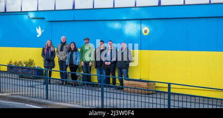 Starbeck, Harrogate, Großbritannien. 10. April 2022. Mitglieder der Starbeck Community Group Jill De Witt, Andrew Hart, Lucky Hubbard, Nik Mills, John Keane, David Stead und Colin Wilson fotografierten vor einer 40 Meter langen ukrainischen Flagge, die sie über dem einst schönen und heute verkommenen Harper-Gebäude in der Starbeck High Street gemalt hatten. Dies ist eines von vielen Projekten, an denen sie arbeiten, um ihre lokale Gemeinschaft zu beleben und zu motivieren. Kredit: ernesto rogata/Alamy Live Nachrichten Stockfoto