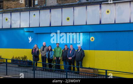 Starbeck, Harrogate, Großbritannien. 10. April 2022. Mitglieder der Starbeck Community Group Jill De Witt, Andrew Hart, Lucky Hubbard, Nik Mills, John Keane, David Stead und Colin Wilson fotografierten vor einer 40 Meter langen ukrainischen Flagge, die sie über dem einst schönen und heute verkommenen Harper-Gebäude in der Starbeck High Street gemalt hatten. Dies ist eines von vielen Projekten, an denen sie arbeiten, um ihre lokale Gemeinschaft zu beleben und zu motivieren. Kredit: ernesto rogata/Alamy Live Nachrichten Stockfoto