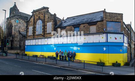 Starbeck, Harrogate, Großbritannien. 10. April 2022. Mitglieder der Starbeck Community Group Jill De Witt, Andrew Hart, Lucky Hubbard, Nik Mills, John Keane, David Stead und Colin Wilson fotografierten vor einer 40 Meter langen ukrainischen Flagge, die sie über dem einst schönen und heute verkommenen Harper-Gebäude in der Starbeck High Street gemalt hatten. Dies ist eines von vielen Projekten, an denen sie arbeiten, um ihre lokale Gemeinschaft zu beleben und zu motivieren. Kredit: ernesto rogata/Alamy Live Nachrichten Stockfoto