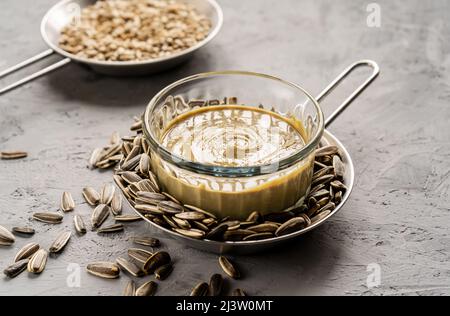 Hausgemachte Sonnenblumenkerne Butter oder mit gerösteten Samen auf grauem Hintergrund verteilt Stockfoto