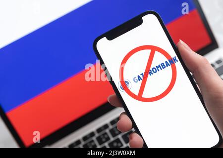 SPB, Russland - 8. April 2022: Gazprombank und Sanktionen. Blockierte russische Bank, Logo und Ban-Symbol auf Handy-Bildschirm und Flagge Hintergrund Stockfoto