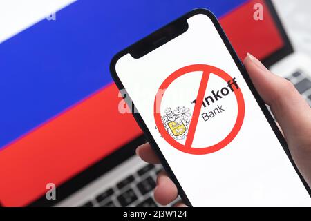 SPB, Russland - 8. April 2022: Tinkoff Bank und Sanktionen. Blockierte russische Bank, Logo und Ban-Symbol auf Handy-Bildschirm und Flagge Hintergrund Stockfoto