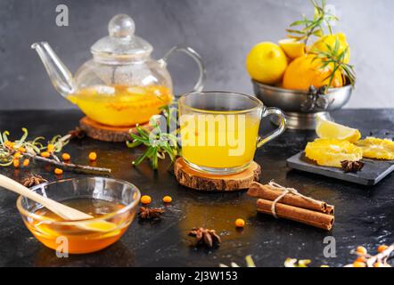 Becher und Teekannen mit Sanddorngetränk aus Honig, Orange, Zitrone, Zimt. Anissterne Stockfoto