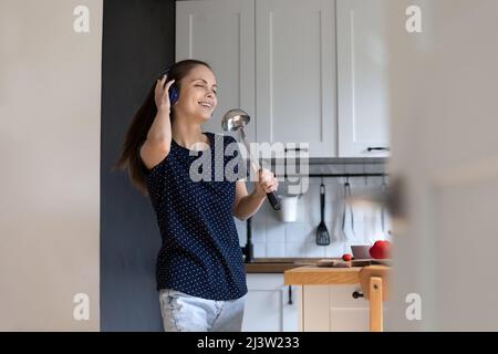 Eine Frau in Kopfhörern hält die Schöpfkelle, als ob sich mike beim Singen sorglos anfühlt Stockfoto