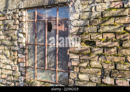 Ein altes Metallfenster mit zerbrochenem Glas an der Wand eines alten verfallenen verlassenen Hauses. Stockfoto