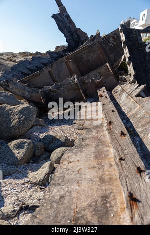Selektiver Fokus auf den zerfallenden Fiberglas-Teil des Rumpfes eines alten Schiffswracks, der zwischen Felsen gestrandet ist Stockfoto