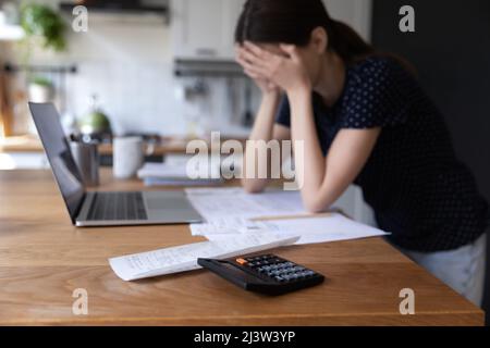Nahaufstellerrechner und Rechnungen auf dem Tisch, verzweifelte Frau auf dem Hintergrund Stockfoto