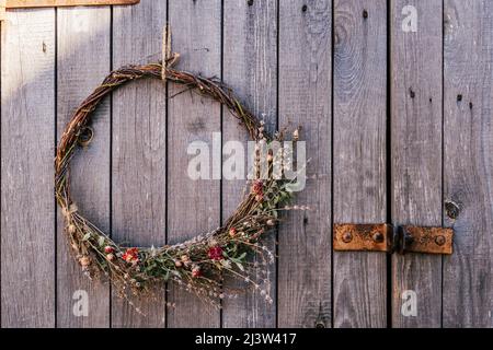Handgefertigter, gedrehter natürlicher, kreativer trockener Kräuterkranz aus Zweigen von Weiden, Wild- und Feldblumen, Getreide und Gras. Traditionelle festliche ethnische Dekoration Stockfoto