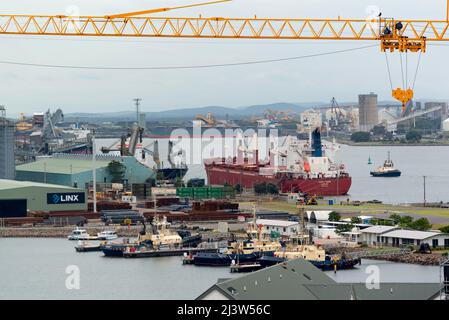 Ein Kranausleger scheint über Schiffen und Schleppern zu schweben, die im Industriegebiet Carrington von Newcastle Harbour, New South Wales, Australien, vertäut sind Stockfoto