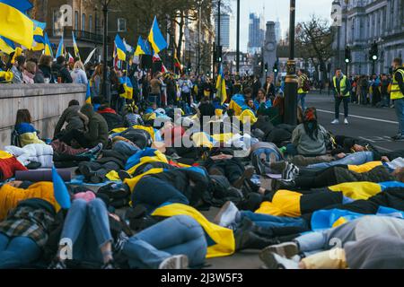 Aus Protest gegen den Krieg Russlands mit der Ukraine liegen Menschen auf dem Boden. Wir bitten darum, den Krieg inmitten ukrainischer Flaggen zu beenden. Demonstration gegen den Krieg Stockfoto