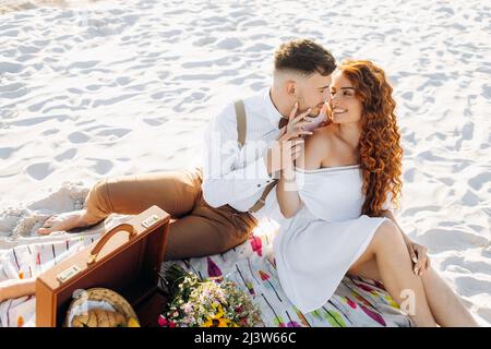 Picknick im Sommer auf dem Sand am See. Schönes junges Paar Stockfoto