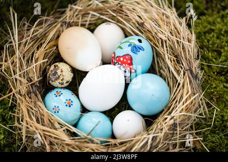 10. April 2022, Bayern, Egloffstein: Bemalte und weiße Ostereier liegen in einem Nest neben einem Osterbrunnen. Nach einer zweijährigen Pause aufgrund der Pandemie werden verächtliche Brunnen wieder zu bunten Kunstwerken: In der Fränkischen Schweiz wurden die ersten Osterbrunnen am Wochenende mit bemalten Eiern und Girlanden aus Tannenzweigen geschmückt. Foto: Nicolas Armer/dpa Stockfoto